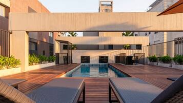 Ein modernes Außenpool-Areal mit Holzdeck und Liegestühlen, umgeben von Gebäuden im minimalistischen Baustil.
