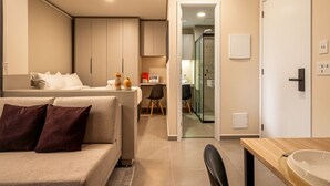 A modern hotel room with a sofa, a dining table, a glass shower, and a kitchenette. - Xtay Vila Madalena (São Paulo)