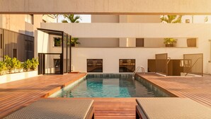 A swimming pool with wooden deck and lounge chairs, surrounded by walls and potted plants. - Xtay Vila Madalena (São Paulo)