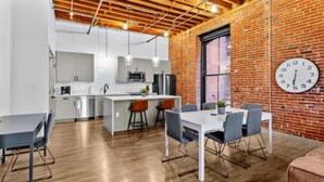 A modern kitchen with white cabinets, a central island, and hanging pendant lights. - Downtown Riverfront Loft Steps from Arch (St. Louis)