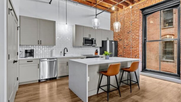 A modern kitchen with white cabinetry, a central island, and two bar stools. - Downtown Riverfront Loft Steps from Arch (St. Louis)
