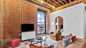 A modern living room with a brick wall, a flat-screen TV, a sofa set, and a coffee table. - Downtown Riverfront Loft Steps from Arch (St. Louis)