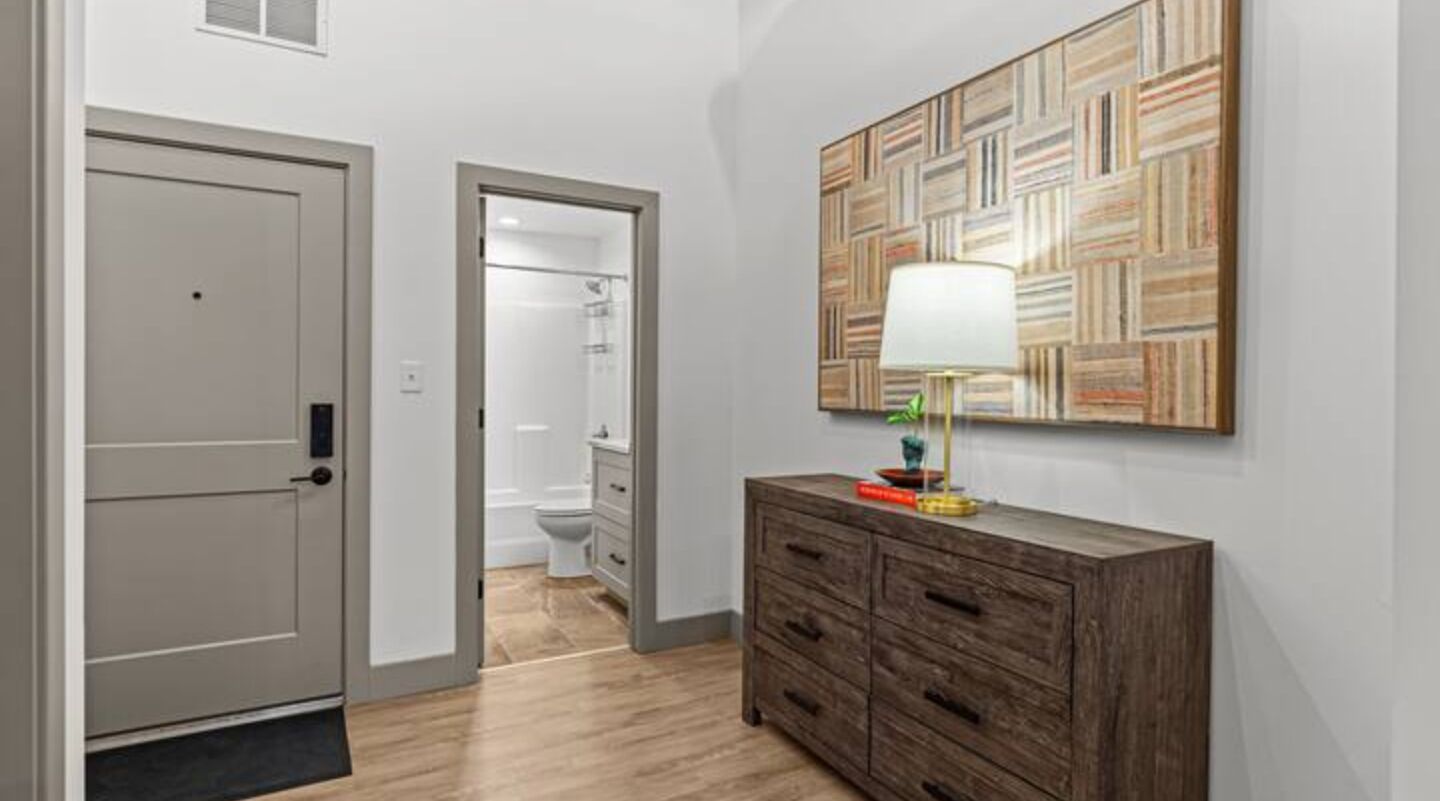 A hallway with a wooden cabinet, a door, and a patterned wall.