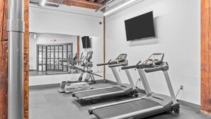 Un gimnasio con cintas de correr, bicicletas estáticas y un televisor en la pared.
