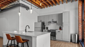 Een moderne keuken met een centraal eiland, grijze kasten, roestvrijstalen apparatuur en een bakstenen muur.