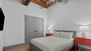 Een slaapkamer met een bed, nachtkastjes, een garderobe en een plafond met zichtbare balken.