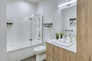 Een moderne badkamer met een douchecabine van glas, een wit toilet, een wastafelmeubel met spiegel en een wastafel.