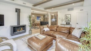A modern living room with a fireplace, leather sofas, a dining area, and a kitchen in the background. - 101 Verbier Building 5 (Mont-Tremblant)