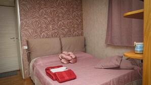 A neatly made bed with a pink bedspread, a floral pillow, and a heart-shaped pillow.