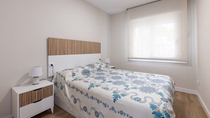 Un dormitorio con cama, mesita de noche, lámpara y ventana con persianas.