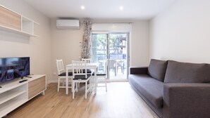 Una sala moderna con un televisor de pantalla plana, un sofá gris, un comedor con sillas blancas y un puerta corrediza de vidrio que da a un patio exterior.