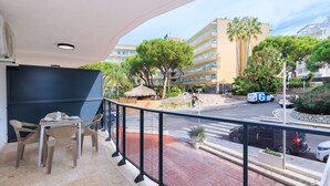 Un balcón con mesa y sillas, con vista a una calle con palmeras y un edificio al fondo.