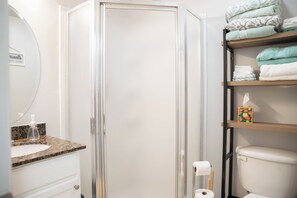 A bathroom with a glass shower enclosure, a sink with a granite countertop, and shelves with folded towels. - Water Views! Pool & hot tub - 2be/2ba condo in Ocean Springs! Harbor Landing (Ocean Springs)