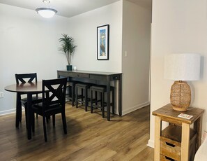 A dining area with a wooden table and chairs, a small plant, and a framed picture on the wall. - Water Views! Pool & hot tub - 2be/2ba condo in Ocean Springs! Harbor Landing (Ocean Springs)