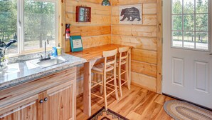Interno di una cabina con angolo cottura, pareti in legno, uno sgabello da bar e una porta che dà sull'esterno.