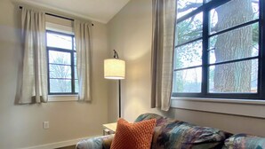 A living room with a patterned sofa, a lamp, and large windows with curtains.