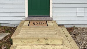 A green door with a window to the right, a wooden front step, and a 'Hello' mat.