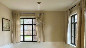 A dining area with a wooden table, a chandelier, and a window with curtains.