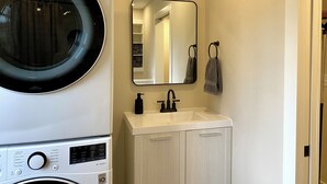 A compact laundry area with a front-loading washer and dryer, a sink with a mirror above it, and a towel hanging on a hook.