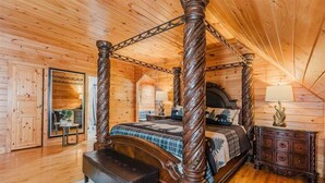Een kamer in een blokhut met een hemelbed, houten vloer en een spiegel aan de muur.