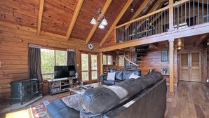 Ein Holzblockhaus-Interieur mit einer großen Couch, einem Kamin, einem Fernseher und einer Treppe, die in einen oberen Bereich führt.
