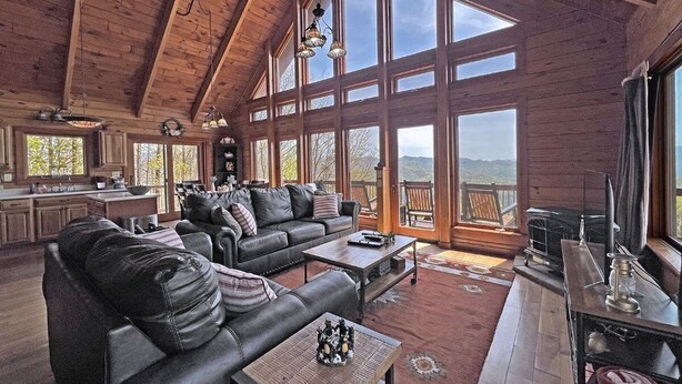 Ein geräumiges Wohnzimmer mit einer großen Holzdachkonstruktion, einer Ledersitzgruppe, einem Couchtisch und Blick ins Freie durch große Fenster.
