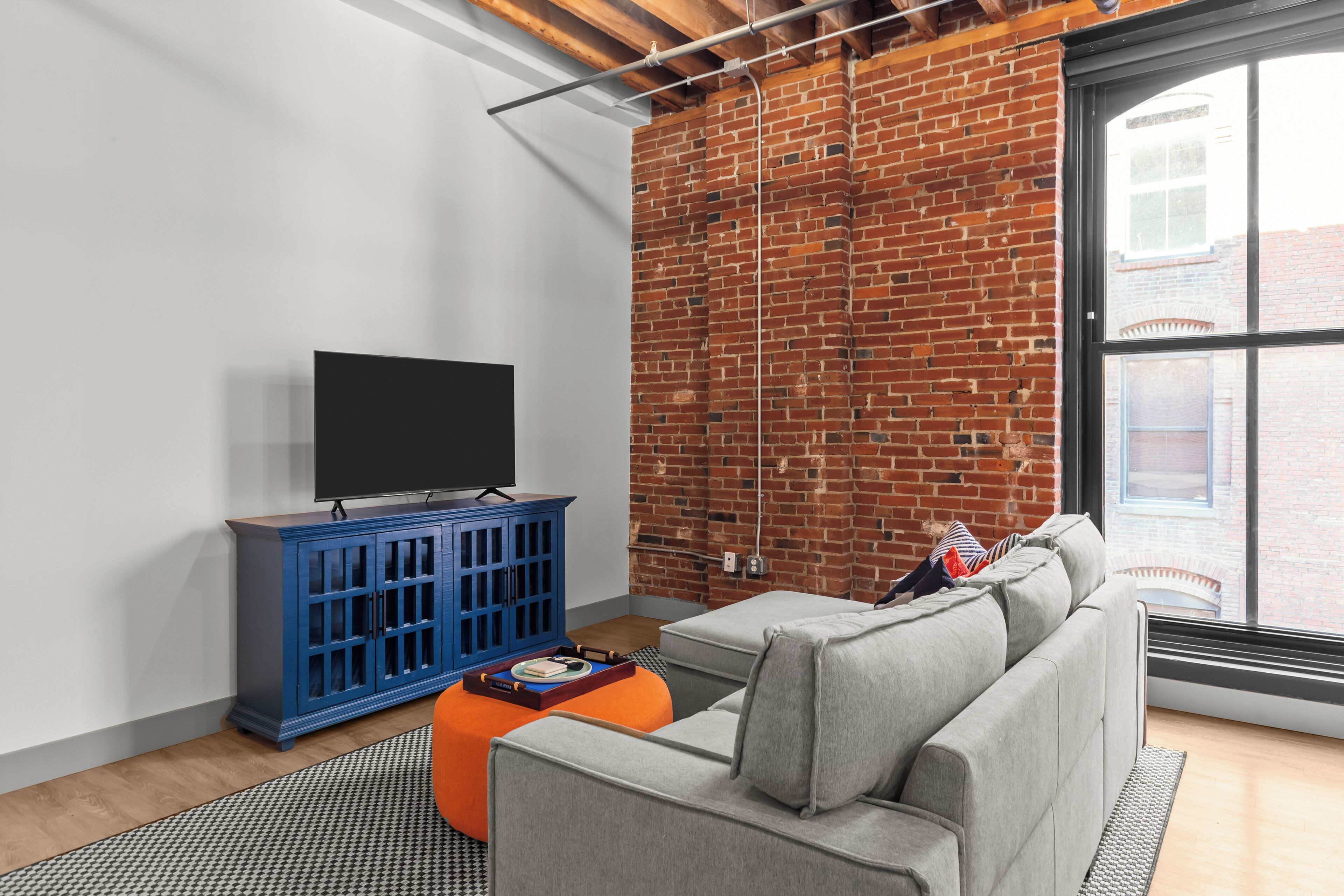 A living room with a grey sofa, a blue cabinet, and a brick wall.