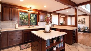 A spacious kitchen with wooden cabinets, a large island, and a view of the outdoors through the windows. - Modern Smoky Mountain Cabin for Big Views, Lake Days, and Hot Tub Nights (Bryson City)