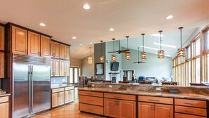 Una cocina moderna con armarios de madera, un refrigerador de acero inoxidable, encimeras de granito e iluminación colgante.