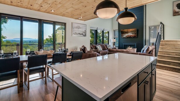 A modern kitchen with a large island, wooden ceiling, and large windows offering a view of the outdoors. - NEW Heated Pool & Theater Luxury Getaway|Mtn Views (Sevierville)