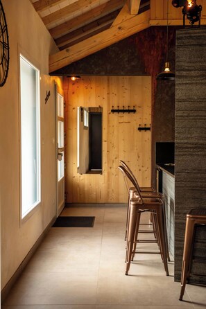 A kitchen with wooden walls, a built-in oven, and a bar area with stools.
