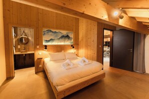A wooden-paneled bedroom with a bed, a painting, and a bathroom visible through an open door.