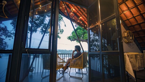 Une pièce dotée d’une porte vitrée donnant sur un balcon avec vue sur des arbres et une étendue d’eau. On y trouve une chaise en osier.