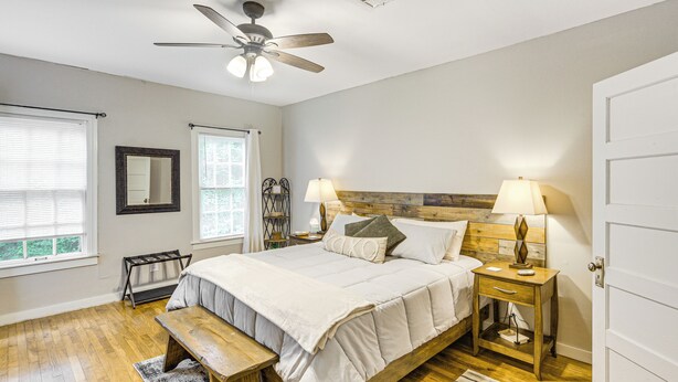 A bedroom with a bed, bedside tables, a bench, a ceiling fan, and a door.