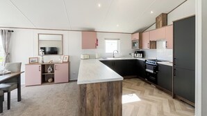 A modern kitchen with a central island, built-in appliances, and a dining area with a table and chairs. - 2 bedroom accommodation in Southerness (Southerness)