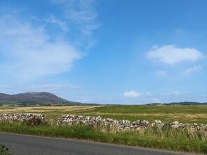 A rural landscape with a stone wall, open fields, and distant hills under a clear sky.