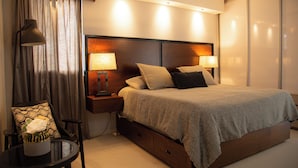 Una moderna camera d'albergo con un letto grande, due comodini con lampade, un tavolino rotondo con un vaso e una sedia con un cuscino decorato.