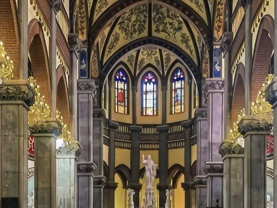 A church interior with arched ceilings, stained glass windows, and statues.