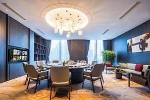 Une salle de conférence moderne équipée d’une table ronde, de chaises, d’un lustre, d’un écran de télévision et d’un canapé.