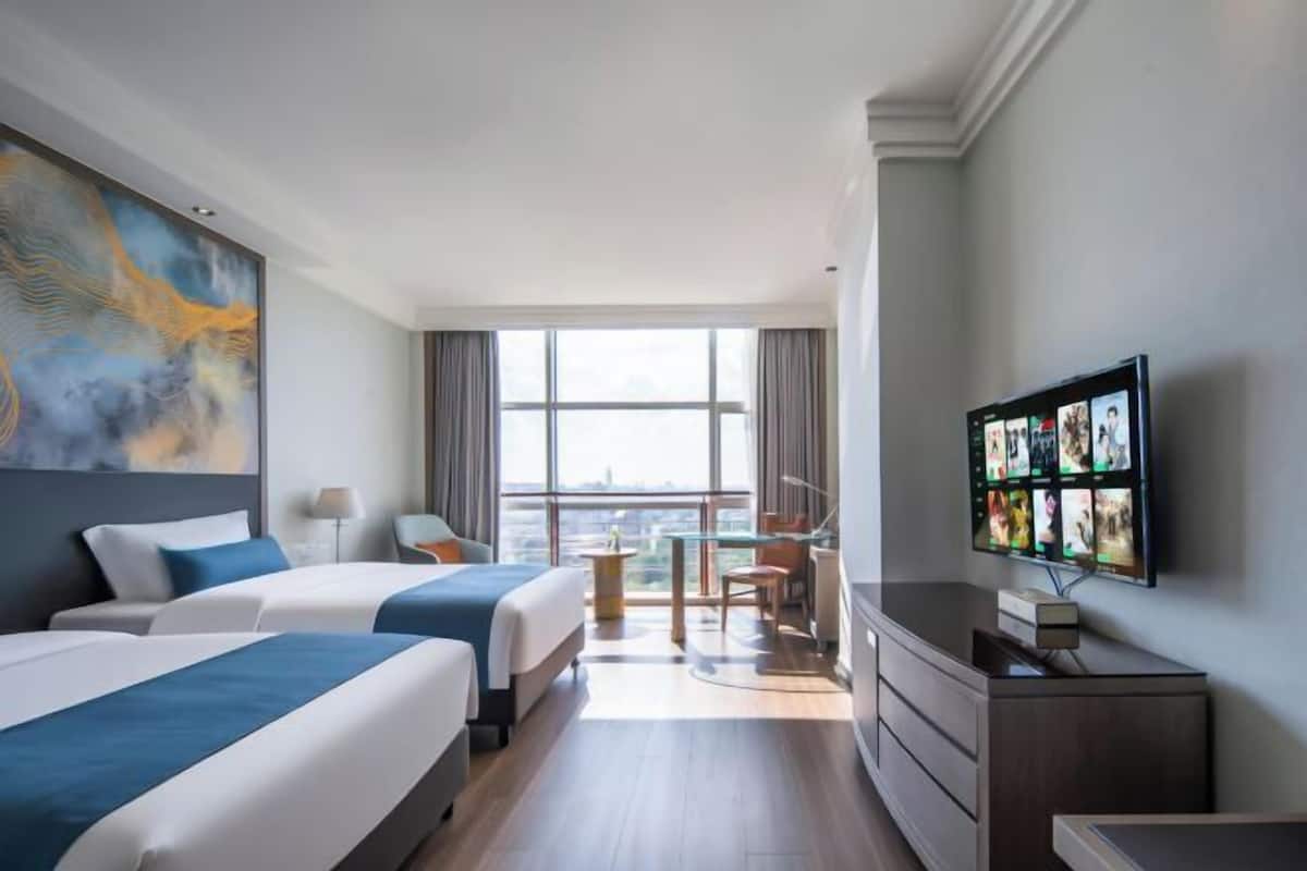 Een hotelkamer met twee bedden, een televisie, een bureau en een groot raam.