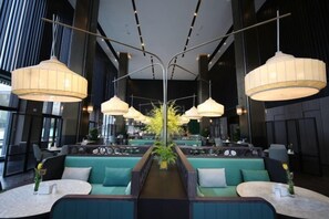 Ein modernes Interieur mit Sitzbereichen, Pendelleuchten und einer zentral platzierten Pflanze.
