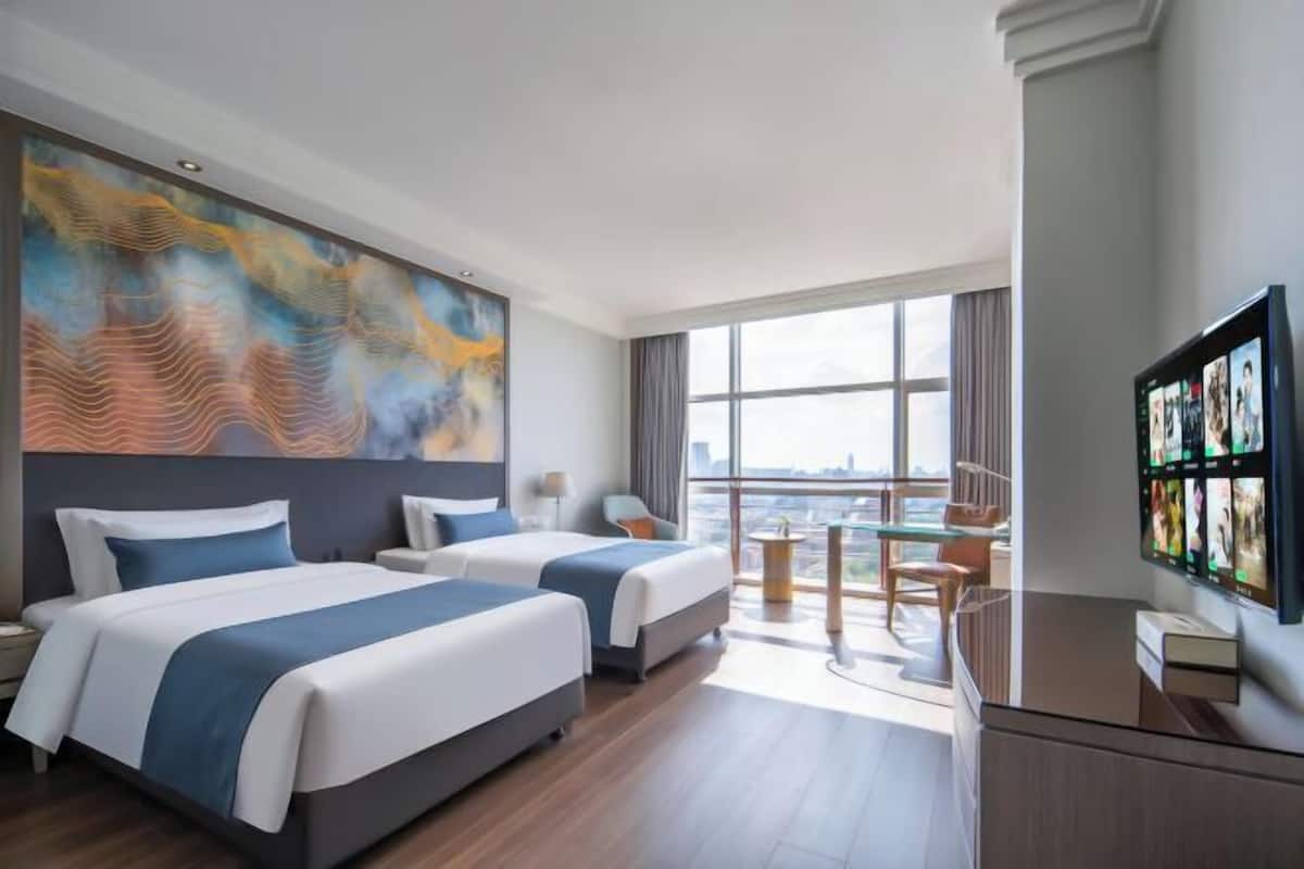 Een hotelkamer met twee bedden, een groot raam, een bureau en een televisie.
