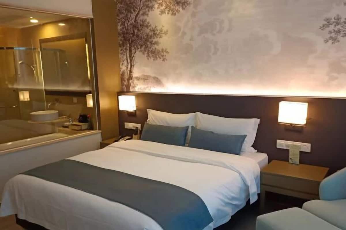 Een hotelkamer met een groot bed, twee nachtkastjes, een spiegel en een wanddecoratie.