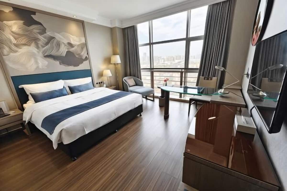 Een hotelkamer met een groot bed, een bureau, een stoel, een televisie en uitzicht op de stad.