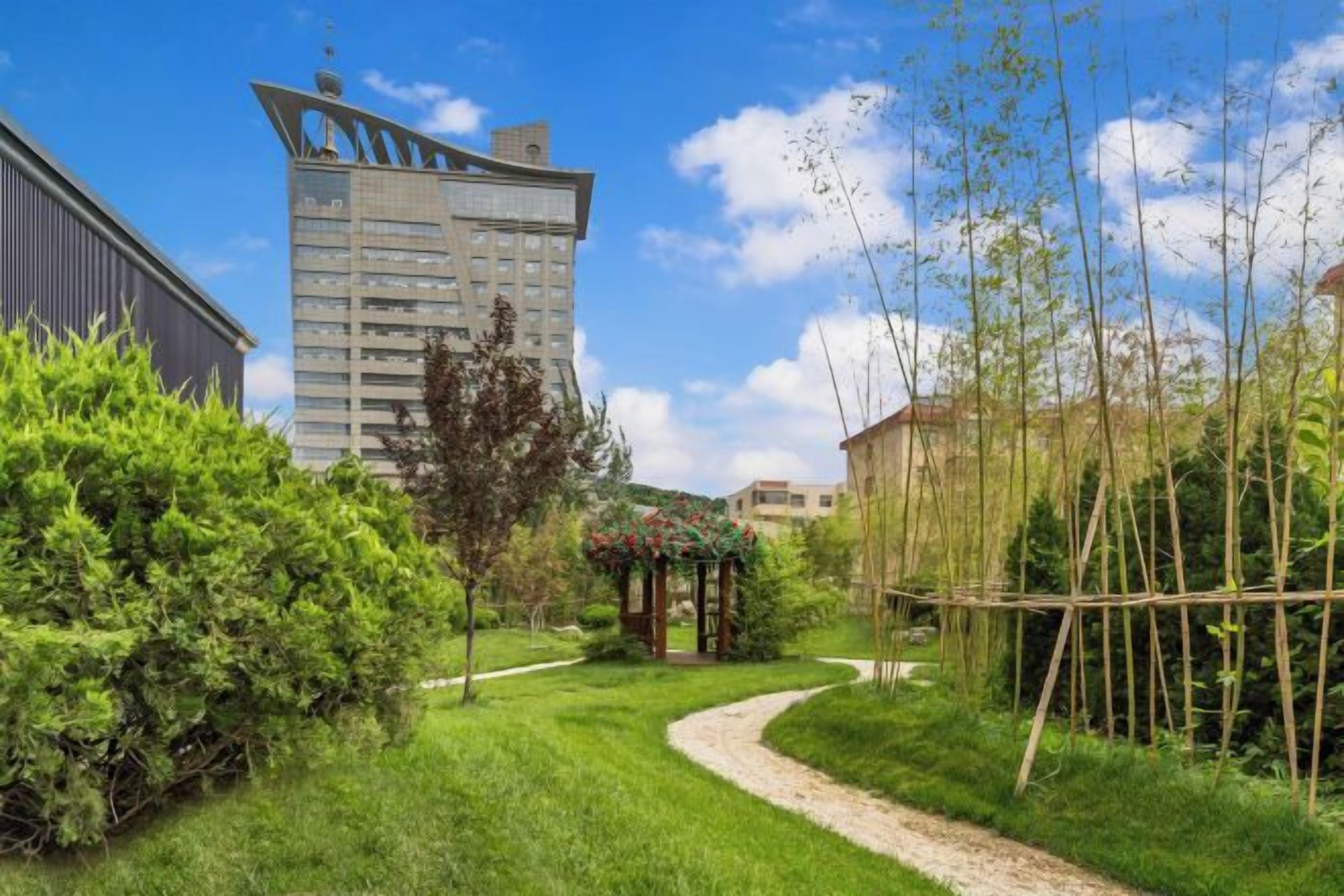 Un camino conduce a un pabellón en un jardín cuidado, con un edificio moderno al fondo.
