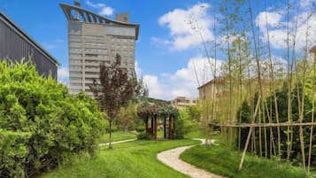 Un camino conduce a un pabellón en un jardín cuidado, con un edificio moderno al fondo.