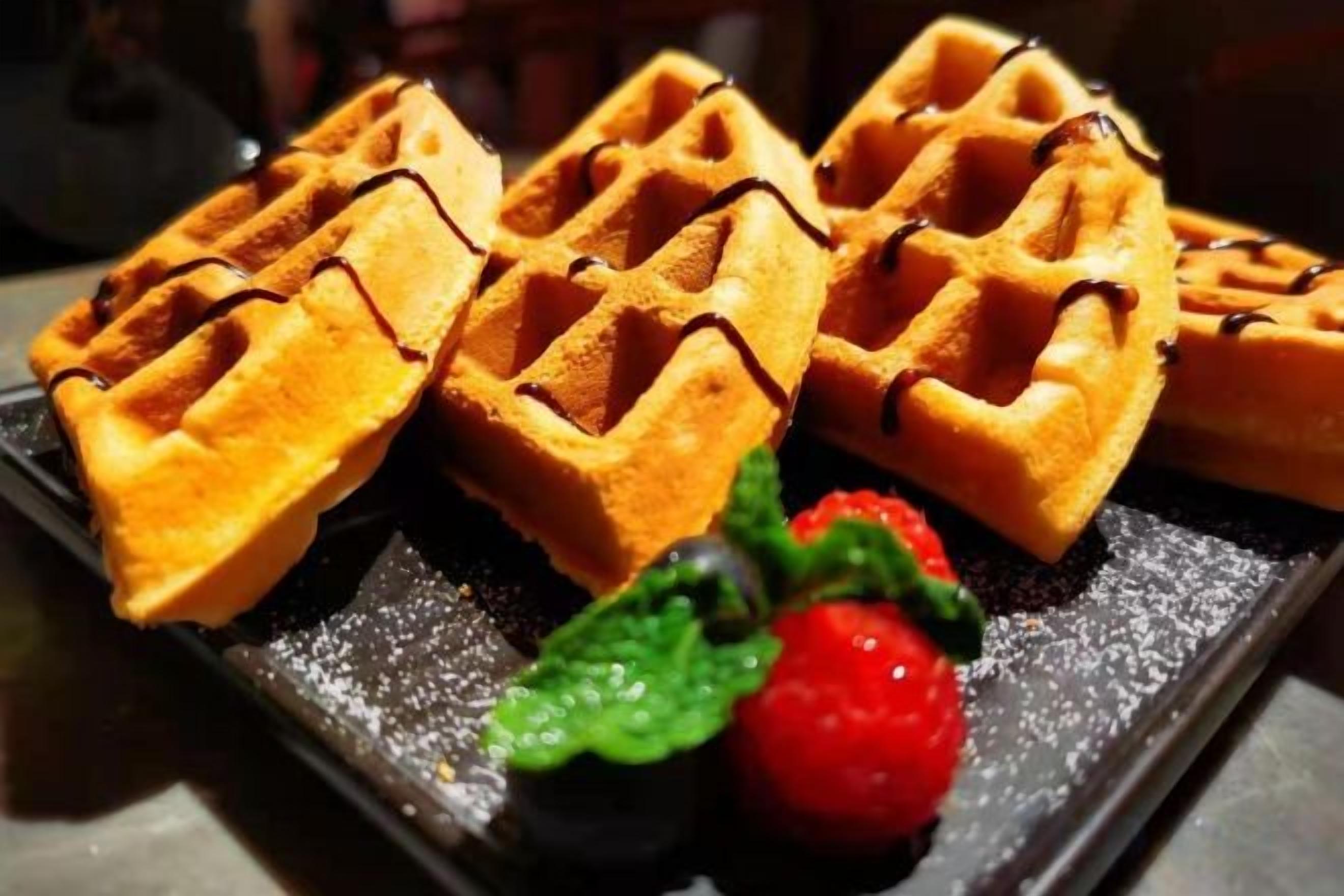 A tray of waffles with chocolate drizzle and a strawberry.