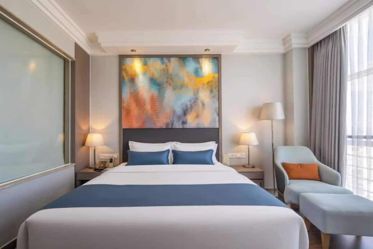 Hotelkamer met een groot bed, twee nachtkastjes met lampen, een fauteuil en een groot abstract schilderij aan de muur.