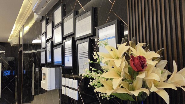 A reception area with a black marble wall, framed certificates, and a floral arrangement. - Marin Suite Al-Badiah Serviced Apartments  (Riyadh)
