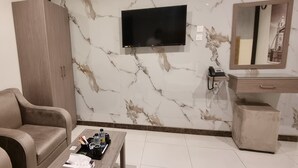 A modern hotel room with a sofa, a coffee table with amenities, a TV, a mirror, and a wardrobe. - Marin Suite Al-Badiah Serviced Apartments  (Riyadh)